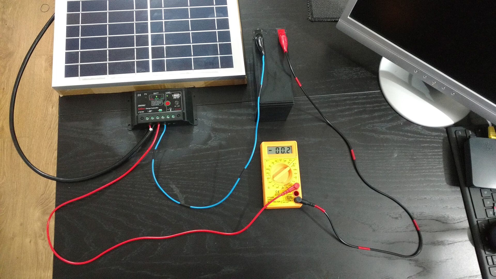 Solar panel, charge controller, battery and multimeter wired together on a desk