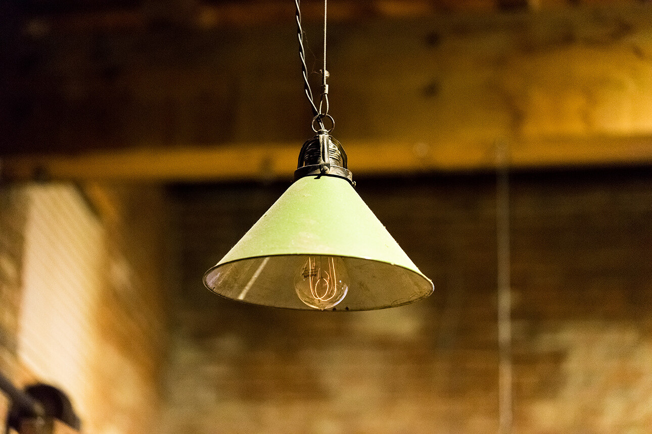 A green enamel lampshade hanging over a filament bulb