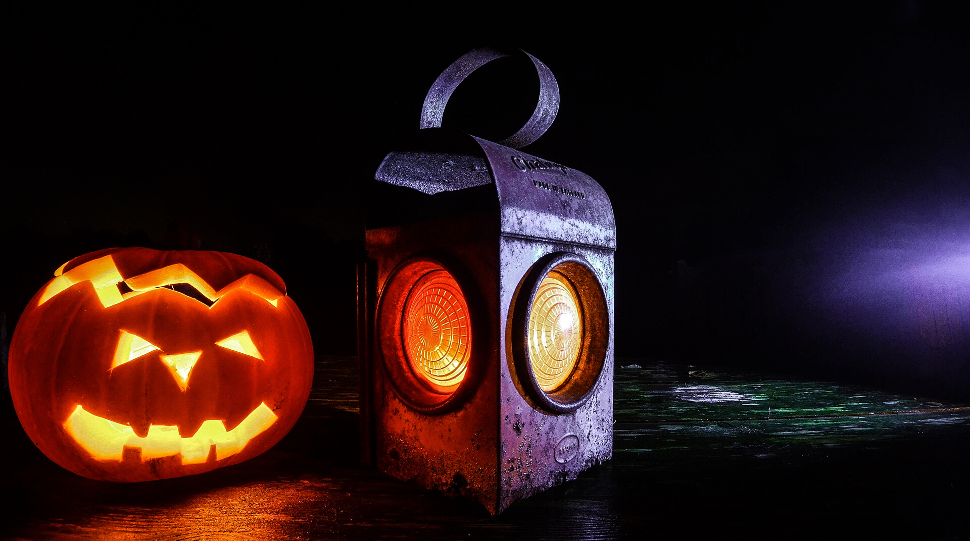 A carved pumpkin and a metal lantern glowing in the dark