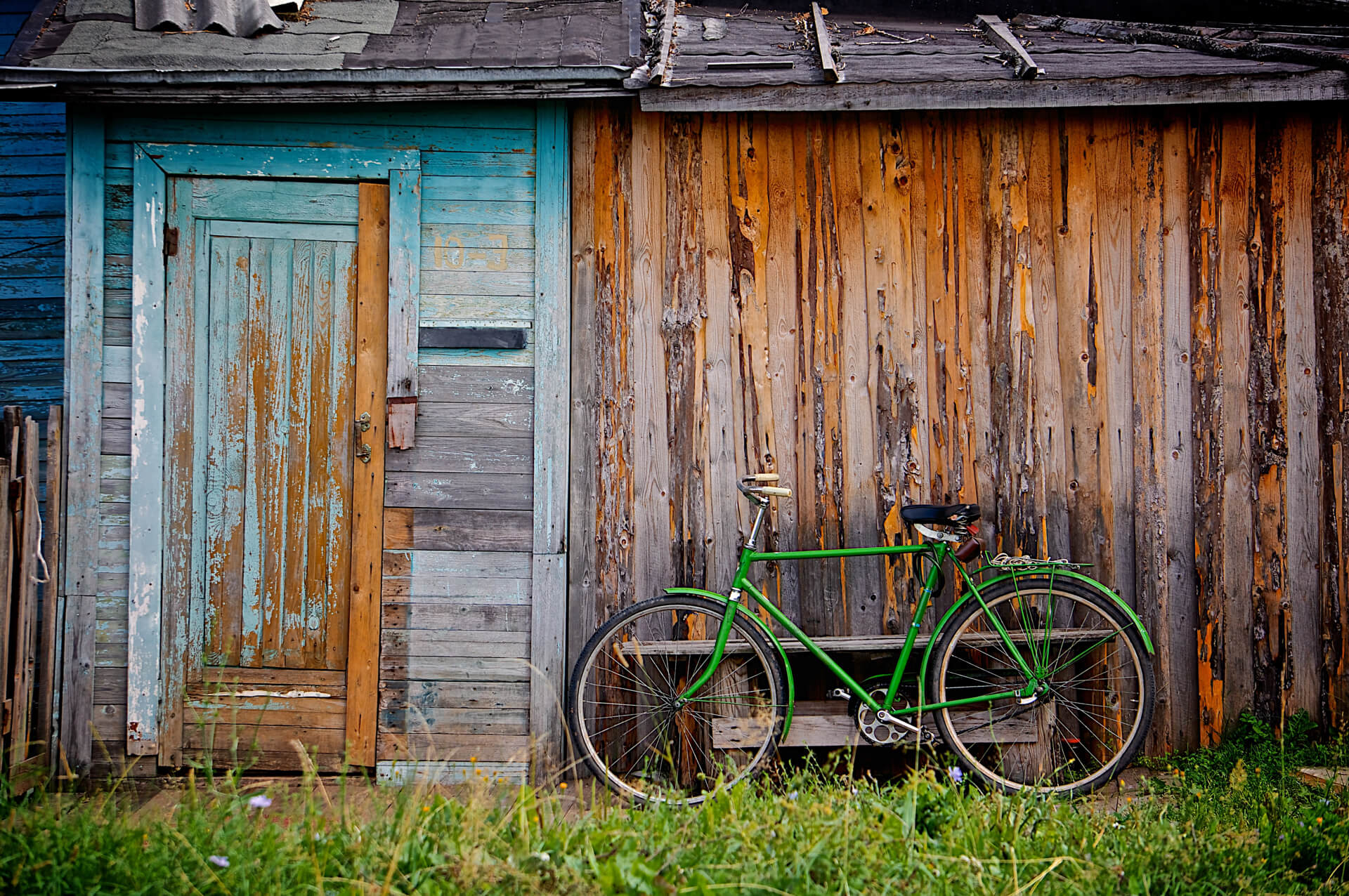 A green bicycle leaning against an old weathered wooden shed