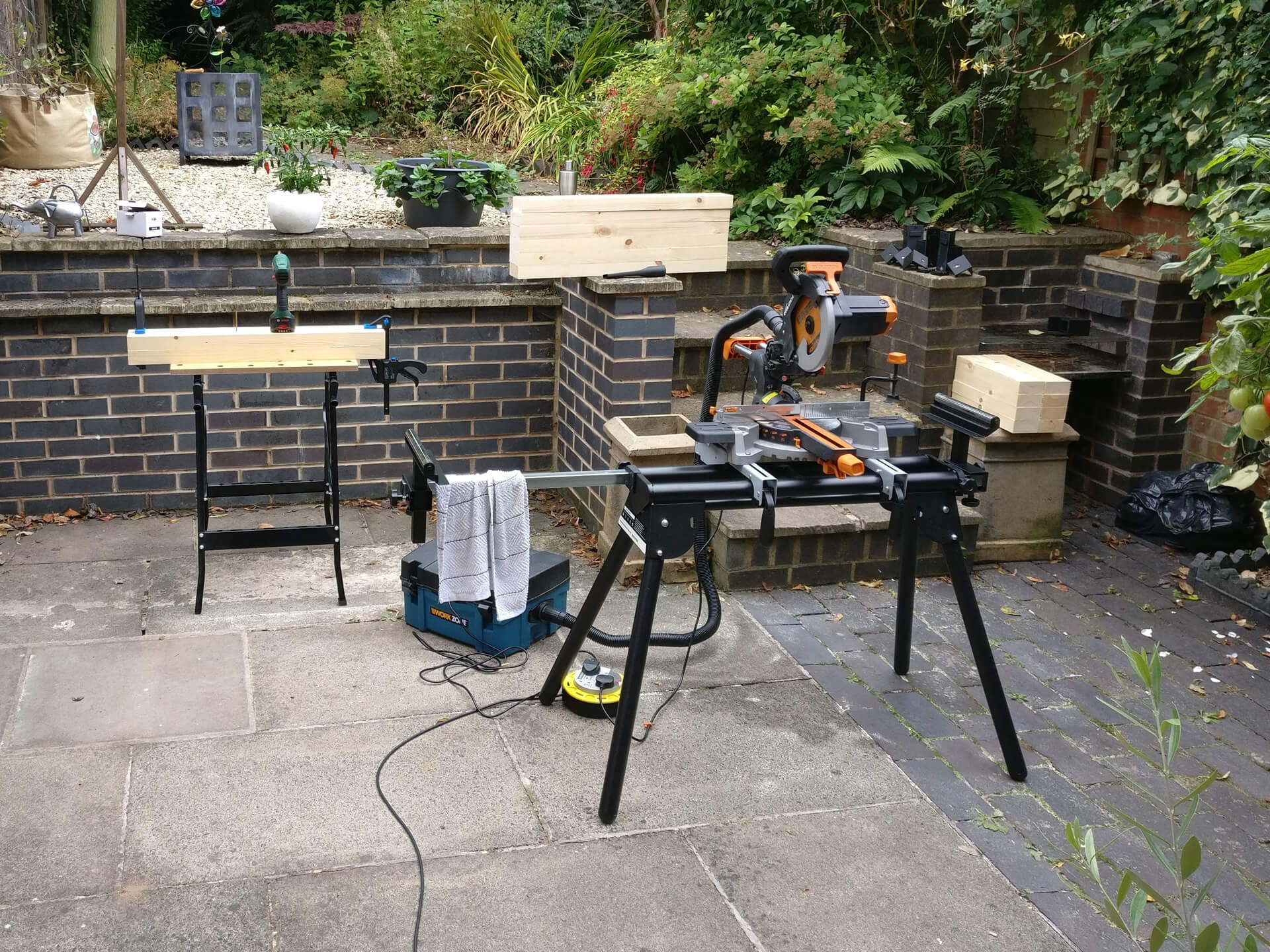 The mitre saw on its stand in the garden, next to a folding workbench