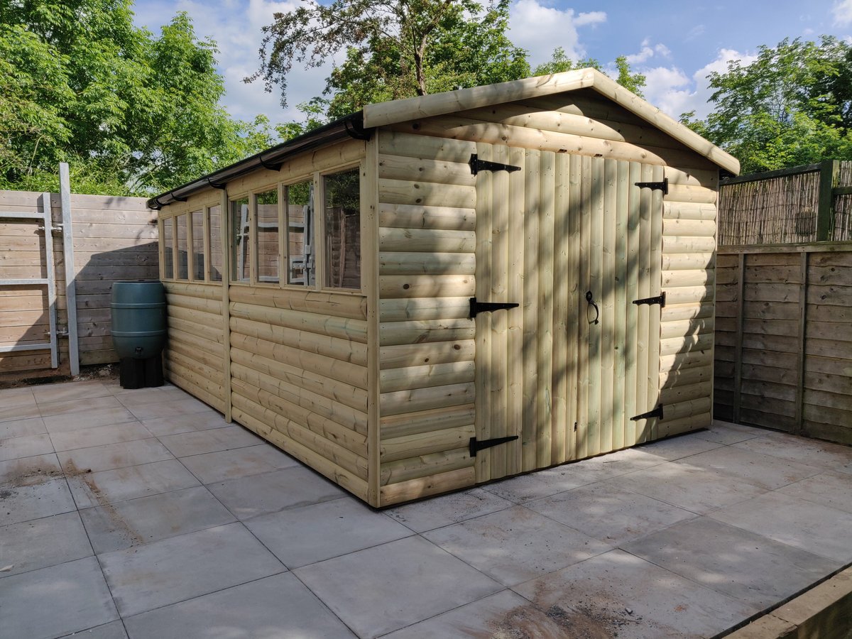 The finished workshop, a timber building with a row of windows and double doors, on its paved base