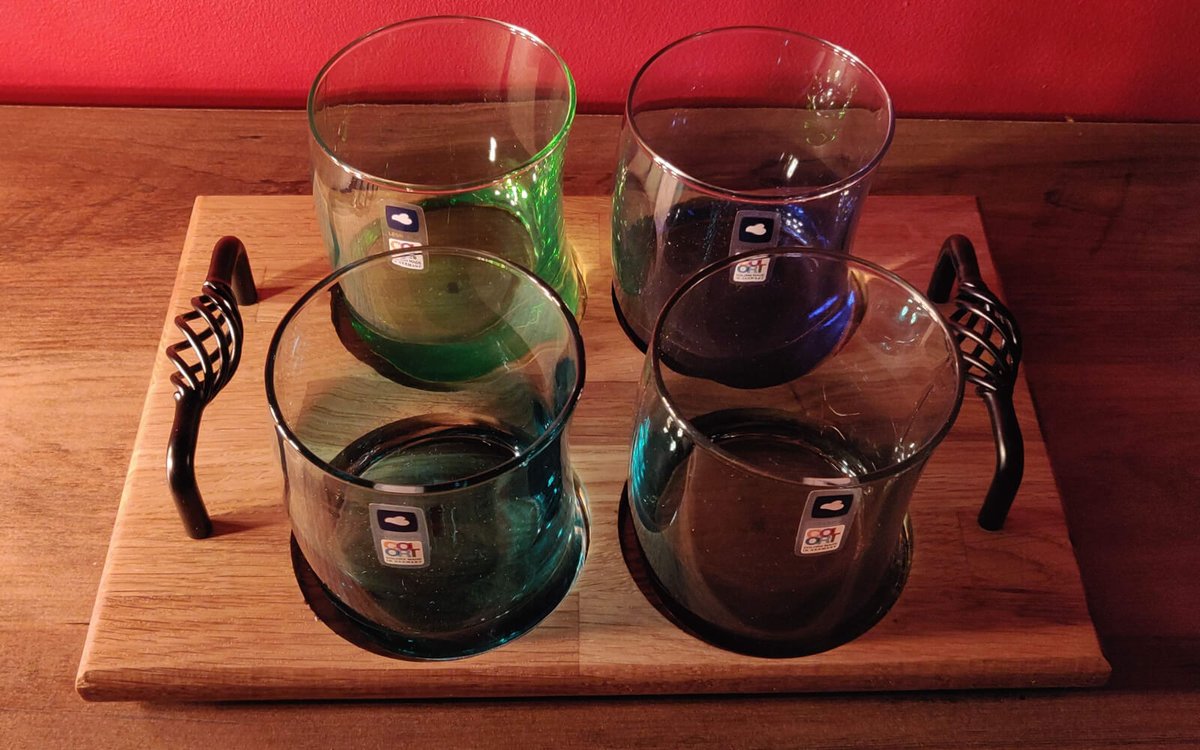 Four coloured tumblers sitting in an oiled oak flight paddle with twisted black metal handles at each end