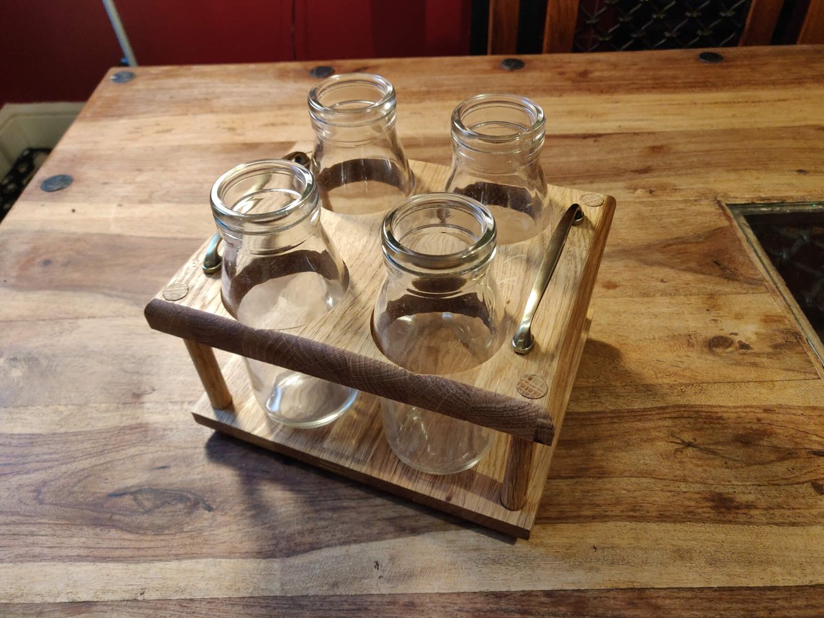Four glass milk bottles in an oak caddy with brass handles and a rounded oak carrying rail