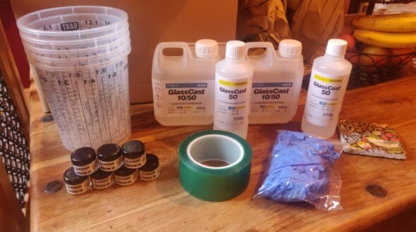 GlassCast resin bottles, mixing cups, pigment pots, green flash tape and a bag of nitrile gloves on a table
