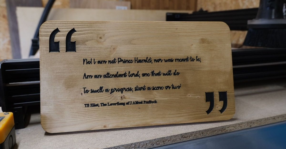 A pine board carved with three lines from The Love Song of J. Alfred Prufrock in script, with large black quotation marks either side