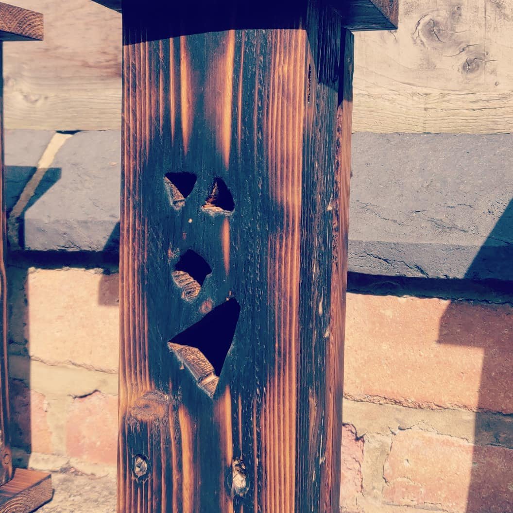 Close-up of one lantern's face: two triangular eyes, a small triangular nose and a crooked mouth cut through the charred pine