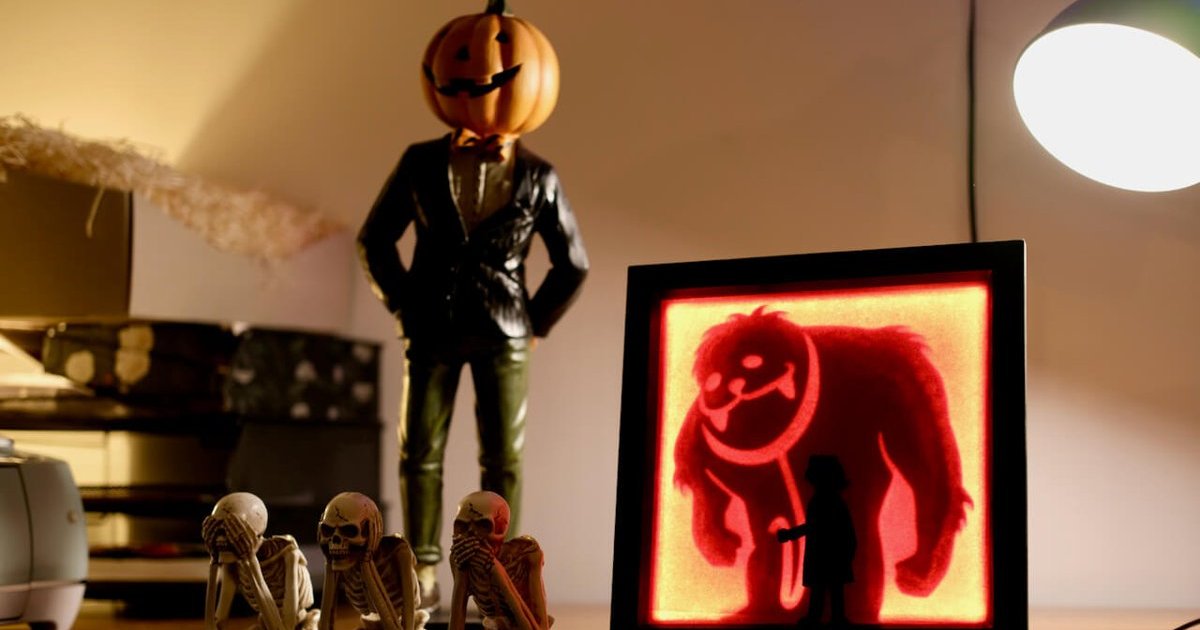 A light box glowing red with a monster silhouette behind a small girl, on a shelf beside skeleton figures and a pumpkin-headed statue
